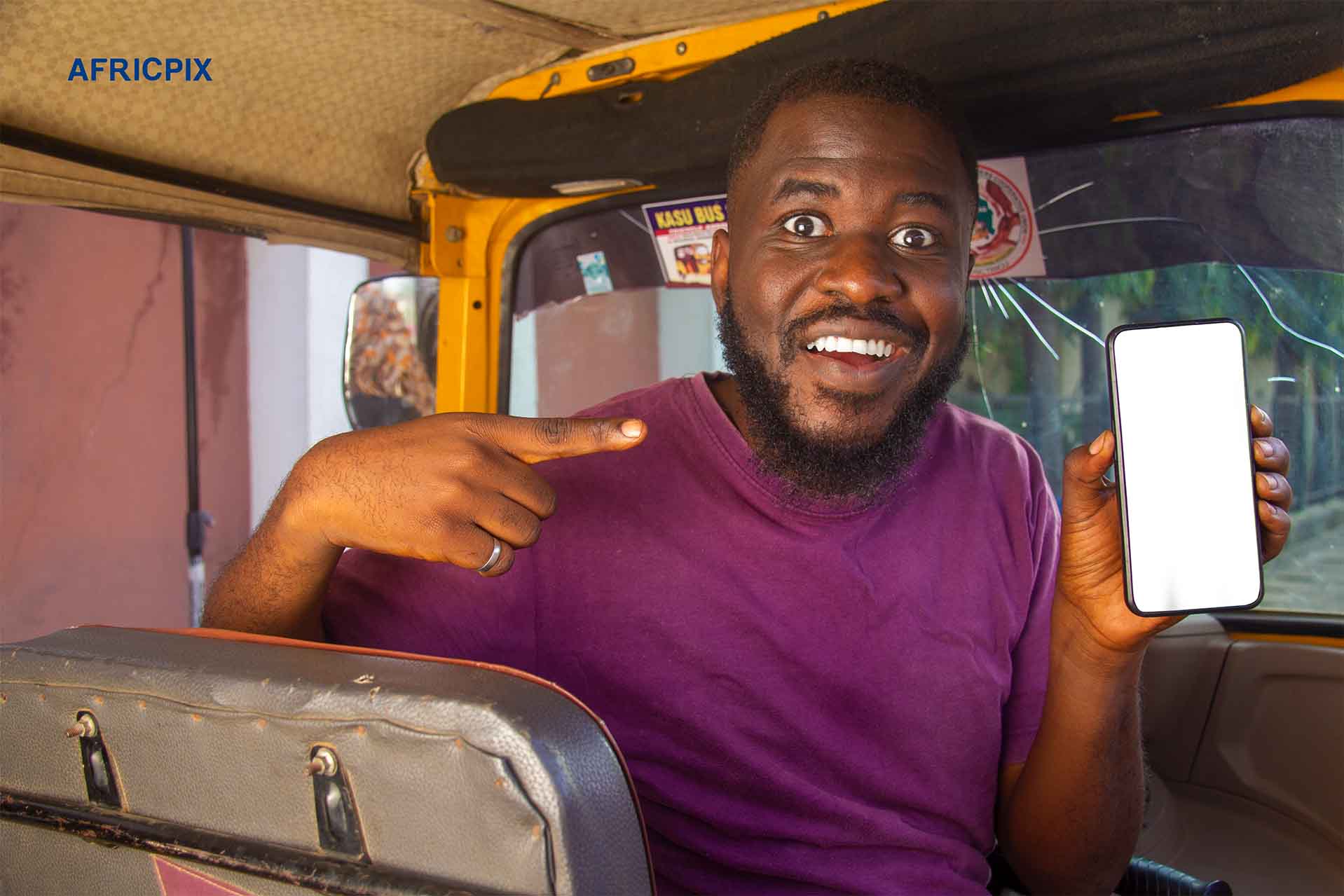 An African man sitting inside a tricycle, keke,maruwa smiling happily while pointing at a phone